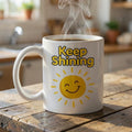 Keepsake lane white ceramic coffee mug with a smiling sun graphic and Keep Shining text on a wooden table