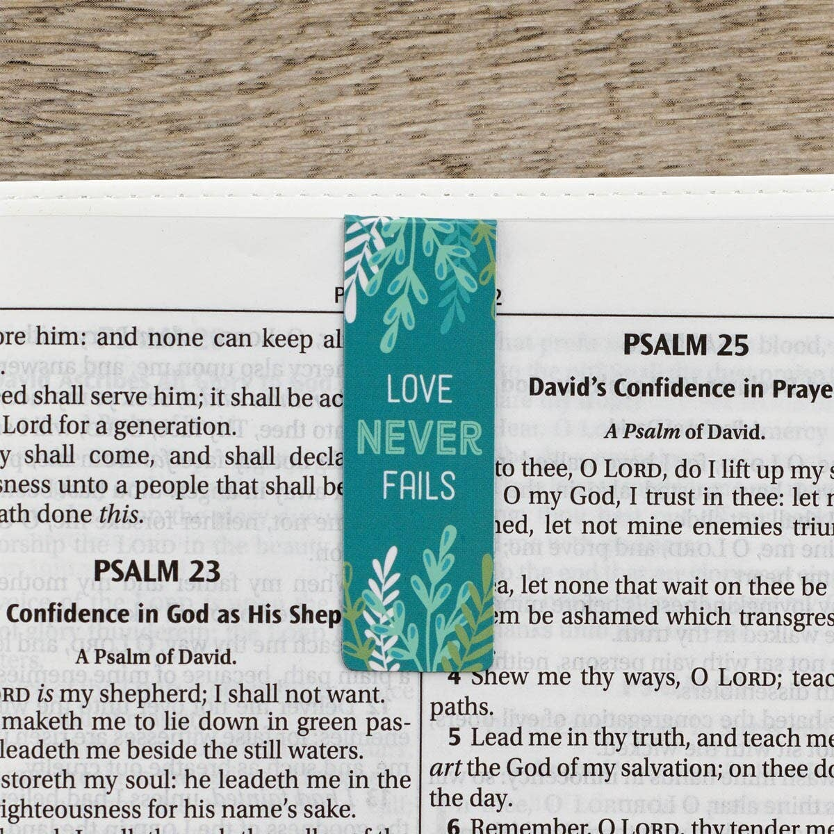 Keepsake lane teal bookmark with white leaf pattern and the inspirational text Love Never Fails resting on a Bible
