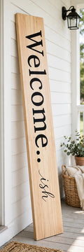 Keepsake lane vertical wooden porch sign with Welcome-ish text in black lettering leaning against a white wall.